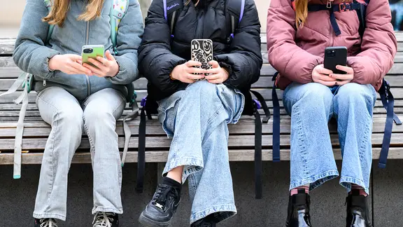 Schüler sitzen auf einer Bank und haben ihre Smartphones in der Hand
