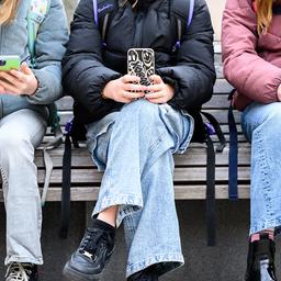 Schüler sitzen auf einer Bank und haben ihre Smartphones in der Hand