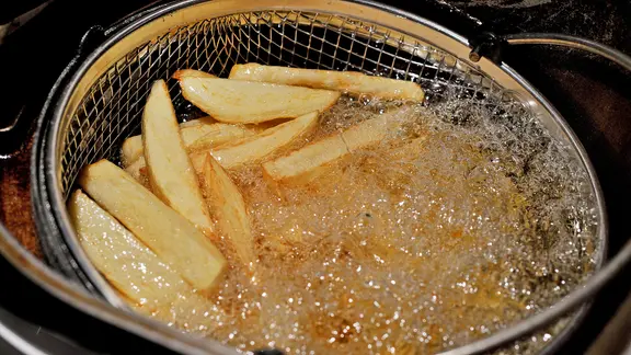 Durch doppeltes Frittieren werden Pommes besonders knusprig. | picture alliance / empics, Nick Ansell Eine Portion Pommes frites schwimmt in einer Fritteuse.