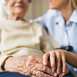 Eine Pflegerin legt den Arm um eine alte Frau im Rollstuhl und hält deren Hand.