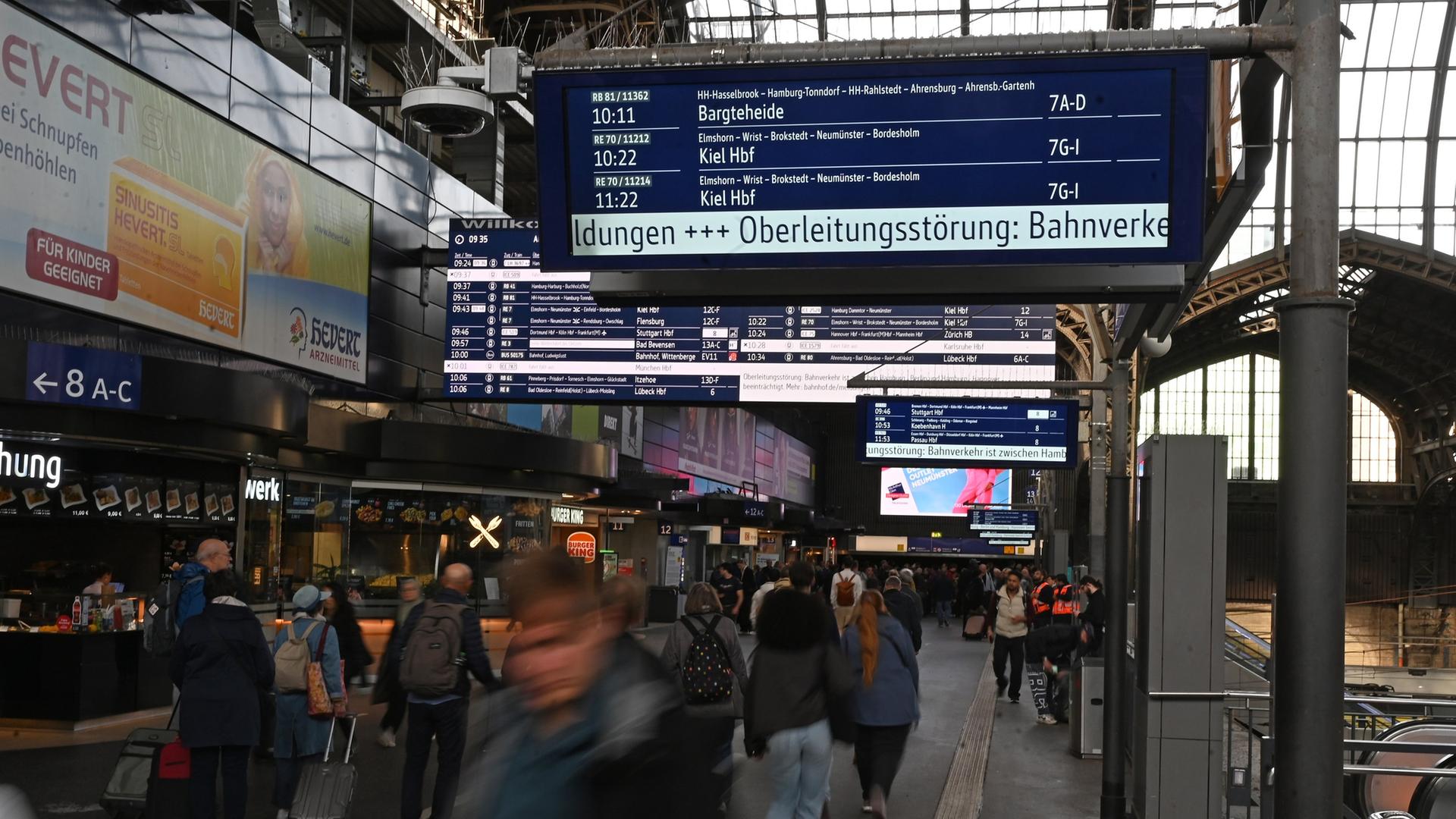 Reisende gehen im Hamburger Hauptbahnhof, während auf einer Tafel der Deutschen Bahn eine Oberleitungsstörung angezeigt wird.  | picture alliance / dpa, David Hammersen
