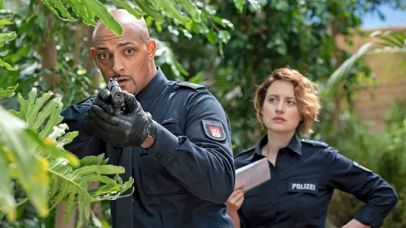 Auf der Suche nach einer Schlange im tropischen Gewächshaus reagiert Lukas Petersen (Patrick Abozen, r.) panisch und zückt seine Waffe. Kollegin Nina Sieveking (Wanda Perdelwitz, r.) hingegen bleibt cool.