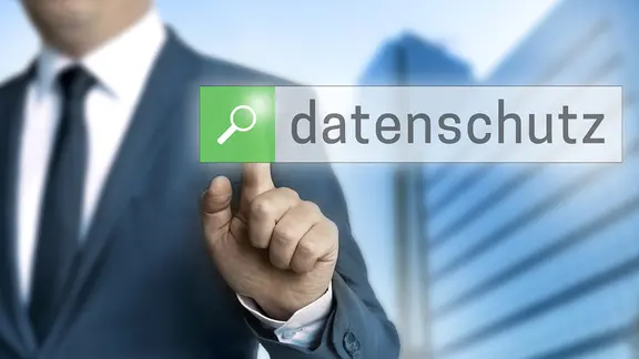 Ein Mann zeigt auf den Begriff "Datenschutz" auf einem Touchscreen an einer Wand.