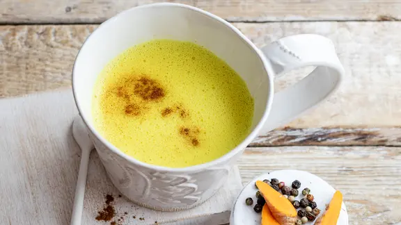 Ein Becher Goldene Milch steht zusammen mit Gewürzen auf einem Tisch. | NDR / ZS Verlage, Claudia Timmann Ein Becher Goldene Milch steht zusammen mit Gewürzen auf einem Tisch.
