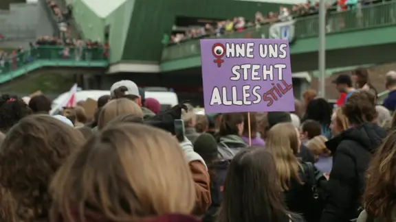 Bei einer Demo zum Weltfrauentag wird ein Schild mit der Aufschrift "Ohne uns steht alles still" hochgehalten.