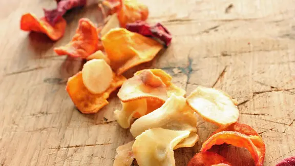 Bunte Gemüsechips auf einem Holztisch.