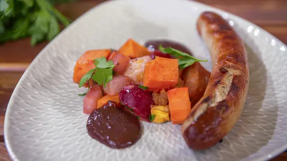 Süßkartoffeln, Kohlrabi und Pflaumen als Beilage zur Bratwurst auf einem Teller angerichtet.