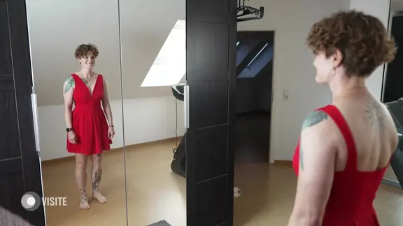 Alexandra in einem roten Kleid vor dem Spiegel. 