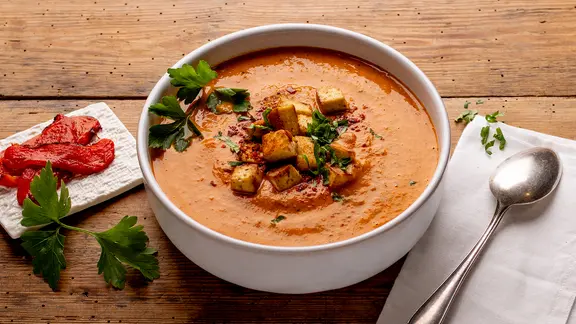 Eine Schale mit einer Paprika-Tomatensuppe, darauf Croutons. 