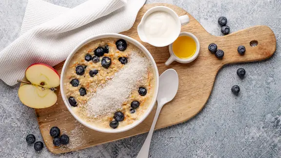 Ein Schälchen mit einem Porridge, garniert mit Heidelbeerenm auf einem Holzbrett. | NDR, Claudia Timmann Ein Schälchen mit einem Porridge, garniert mit Heidelbeerenm auf einem Holzbrett.