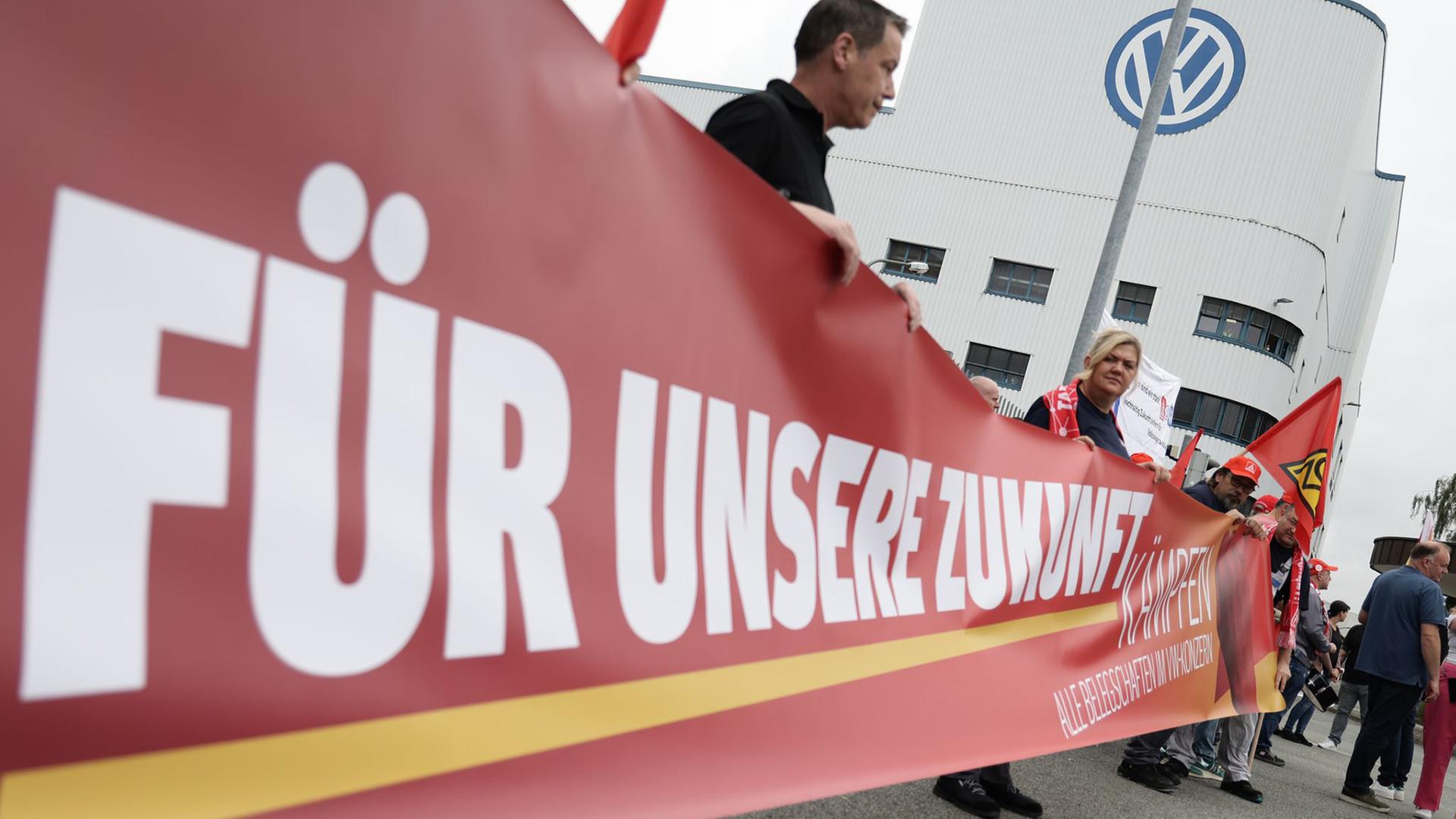 Mitarbeitende von Volkswagen beteiligen sich an einer Informations- und Protestaktion der IG Metall vor dem VW-Werk in Osnabrück. | dpa, David Ebener