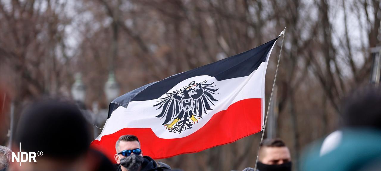 Teilnehmer auf einer Demonstration von Rechtsextremen und Reichsbürgern halten eine Fahne, die an die Reichsflagge erinnert. | picture alliance/Geisler-Fotopress, Jean MW/Geisler-Fotopress Teilnehmer auf einer Demonstration von Rechtsextremen und Reichsbürgern halten eine Fahne, die an die Reichsflagge erinnert.