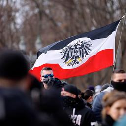 Teilnehmer auf einer Demonstration von Rechtsextremen und Reichsbürgern halten eine Fahne, die an die Reichsflagge erinnert.