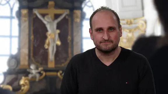 Daniel Kaiser spricht den Hamburg Kommentar vor einem Bild aus dem Innenraum der Hauptkirche St. Michaelis.