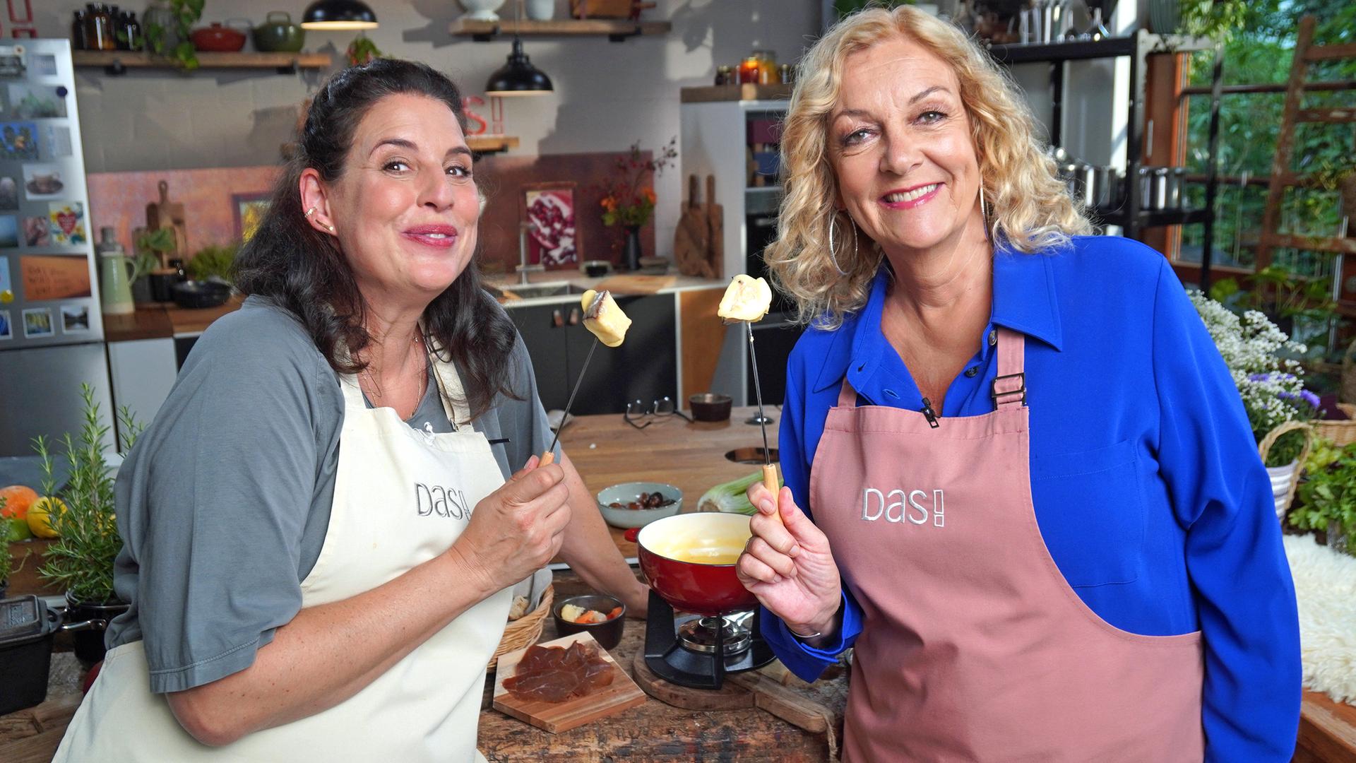 Bettina Tietjen und Elena Uhlig halten Fonduegabeln mit Brot und Käse in die Luft. | NDR,Florian Kruck