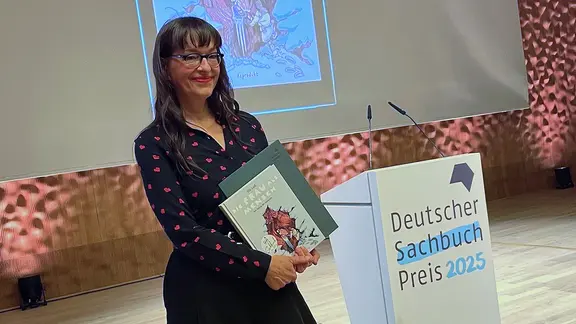 Ulli Lust hält bei der Sachbuchpreisverleihung ihr Buch in den Händen