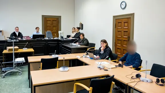 Im Prozess gegen den Hamburger Flughafen-Geiselnehmer sitzt der Angeklagte (r.) im Landgericht im Sitzungssaal neben seiner Rechtsanwältin. Das Gesicht des Angeklagten ist gepixelt.