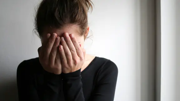 Eine junge Frau schlägt die Hände vor das Gesicht