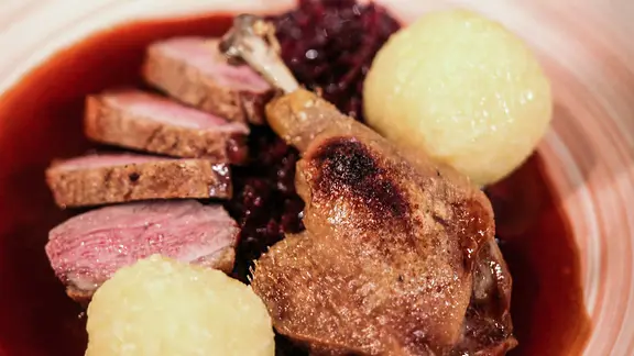 Entenbrust und Entenkeule mit Rotkohl und Kartoffelklößen auf einem Teller angerichtet.