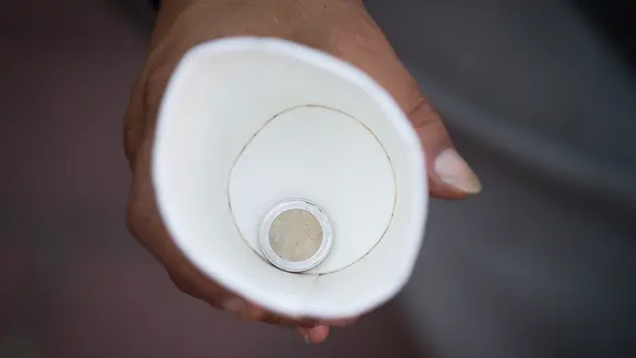 Eine Hand hält einen Becher mit einer 2-Euro-Münze darin.