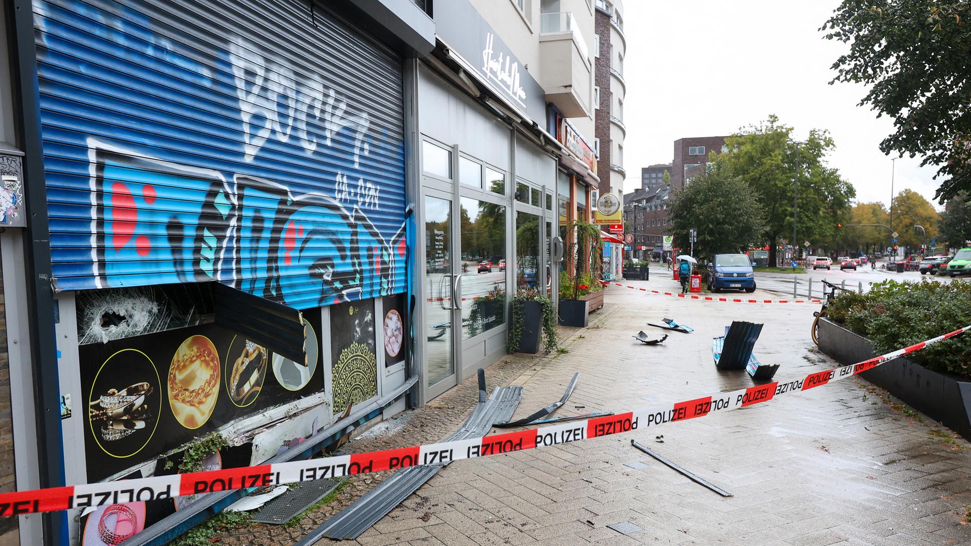 Hinter einer Absperrung der Hamburger Polizei liegen Teile des Rollladens eines Juweliergeschäfts auf einem Gehweg. | picture alliance/dpa/Bodo Marks
