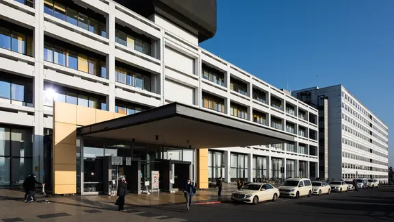View of the main building of the University Medical Center Göttingen with a ward block. Taxis are standing near the entrance, people are walking along a footpath. | picture alliance/dpa, Swen Pförtner View of the main building of the University Medical Center Göttingen with a ward block. Taxis are standing near the entrance, people are walking along a footpath.