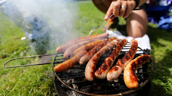 Im Park werden Würstchen auf einem Grill gegrillt.