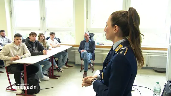 Eine junge Offizierin spricht in einer Schule vor einer Klasse Jugendlicher.