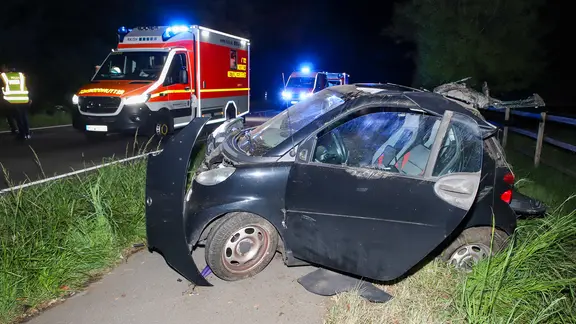 Ein demolierter Zweisitzer steht neben der Fahrbahn, im Hintergrund zwei Krankenwagen.