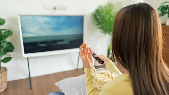 Eine Frau sitzt vor einem Fernseher und hält eine Fernbedienung in der Hand
