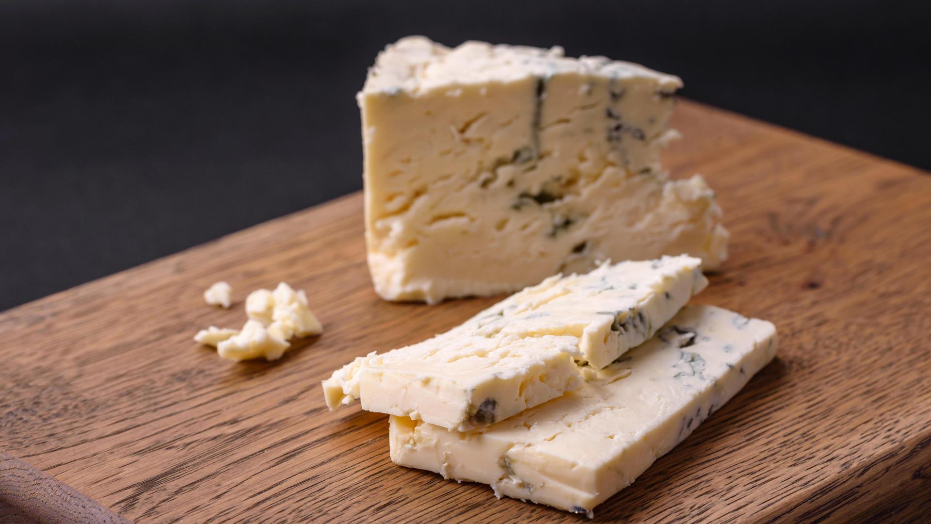 Ein Stück und zwei Scheiben Blauschimmelkäse auf einem Holzbrett. | picture alliance / Zoonar | Tetiana Chernykova