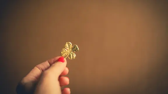 Jemand hält ein vierblättriges Kleeblatt zwischen den Fingern.