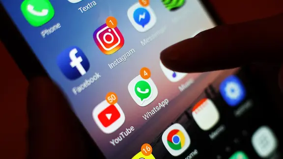 Ein Daumen schwebt über einem Smartphone-Bildschirm mit vielen Social Media Apps.