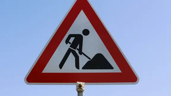 Ein Verkehrsschild vor klarem Himmel weist auf eine Baustelle hin