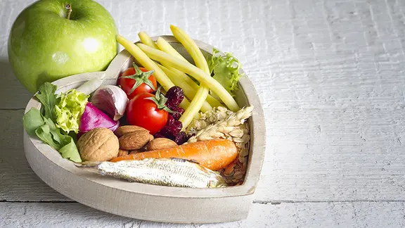 Gemüse und Obst liegen in einer herzförmigen Holzschale.