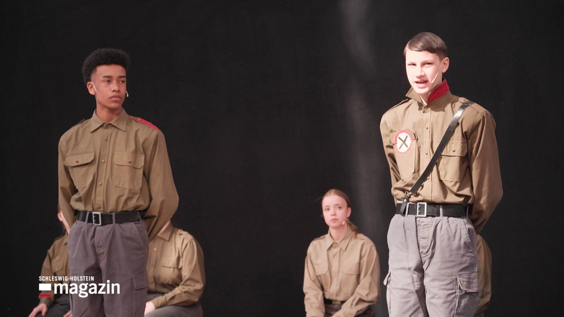 Kinder auf einer Bühne als Nazis verkleidet. | Screenshot