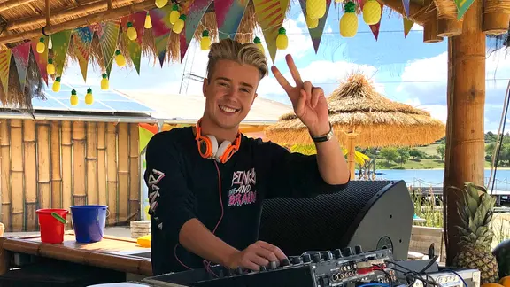 Jaden Bojsen steht hinter einem DJ Pult im Karibik Look.
