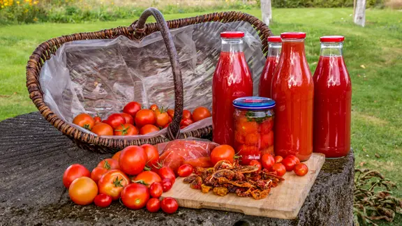 Getrocknete, eingekochte, zu Saft verarbeitete und noch in einem Korb befindliche Tomaten in einem Bild.