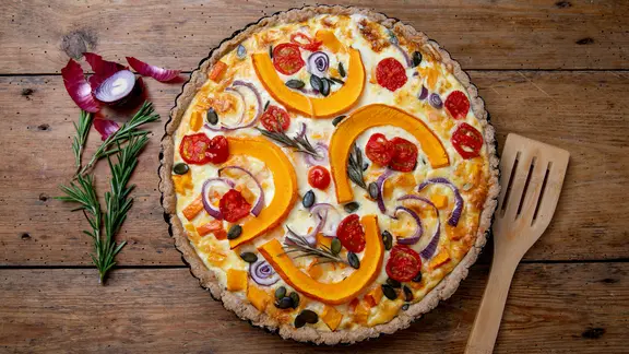 Eine Quiche mit Hokkaido-Kürbis, Tomaten, Zwiebeln und Kürbiskernen.