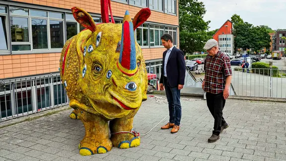 Zwei Männer stehen neben einer knallgelben Nashorn-Skulptur.