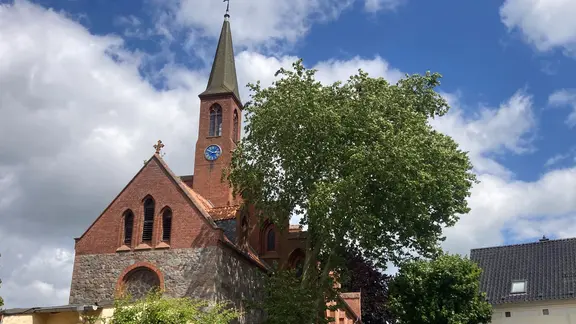 Eine Kirche mit einem Baum im Vordergrund.