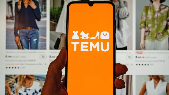 Jemand hält ein Handy mit der Shopping-App Temu vor einen Bildschirm mit Shop-Angeboten.