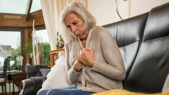 Eine Frau sitzt auf dem Sofa und fasst sich an die Brust.