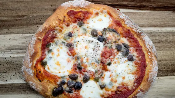 Kartoffelteig-Pizza mit Oliven, Kapern und Sardellen auf einem Untergrund aus Holz | NDR, Tarik Rose Kartoffelteig-Pizza mit Oliven, Kapern und Sardellen auf einem Untergrund aus Holz