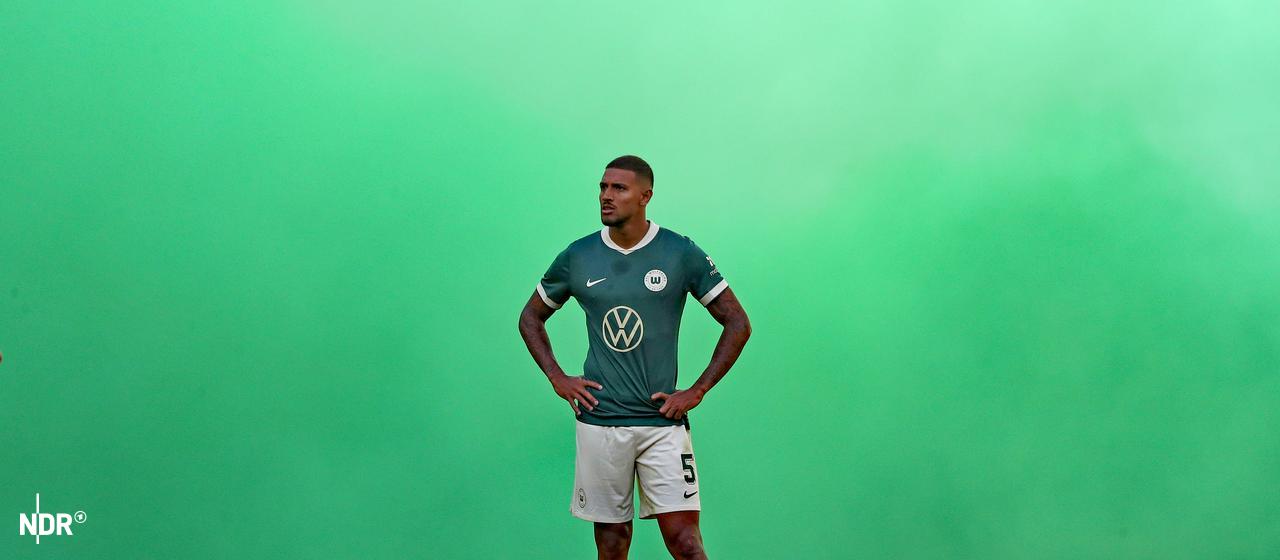 Vinicius Souza vom VfL Wolfsburg steht im grünen Pyro-Qualm