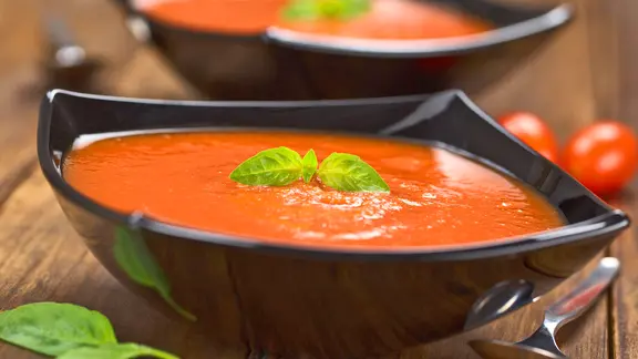 Tomatensuppe in einer schwarzen Suppentasse und mit einem Blatt Basilikum dekoriert.