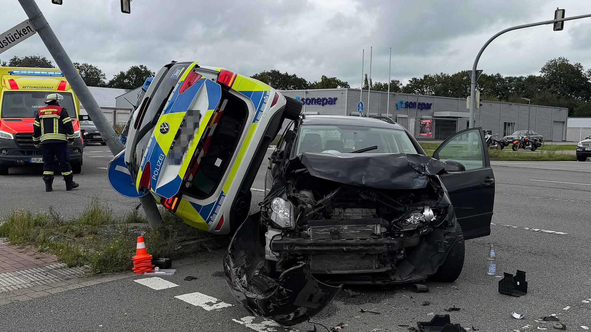 Unfall in Aurich: Ein schwarzes Auto ist stark beschädigt. Zwischen Auto und einem Mast steht schief ein Polizeiwagen. | Diana Stöhr-Aeilts, Freiwillige Feuerwehr Aurich, dpa