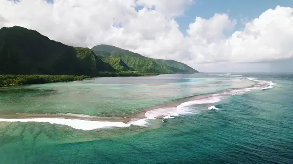 Grüne Berge, ein vorgelagertes Korallenriff und türkisblaues, klares Meer - Landschaftsaufnahme in der Südsee in der Vogelperspektive.