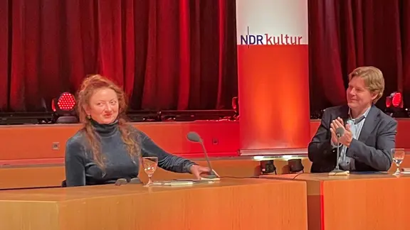 Ο συντάκτης του NDR Jan Ehlert χειροκροτεί τη συγγραφέα Claire Keegan σε ένα βήμα.