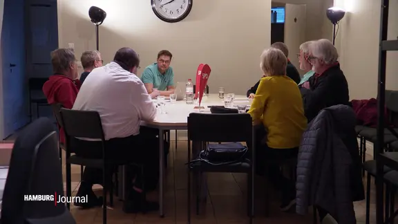 Eine Gruppe von Menschen sitzt in einem Parteibüro um einen runden Tisch herum.